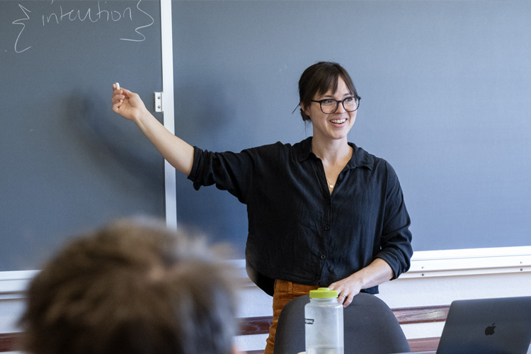 Lucy Vollbrecht teaches class while standing in front of blackboard
